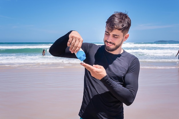 Bell'uomo sulla spiaggia che applica la crema solare per proteggersi dal sole.