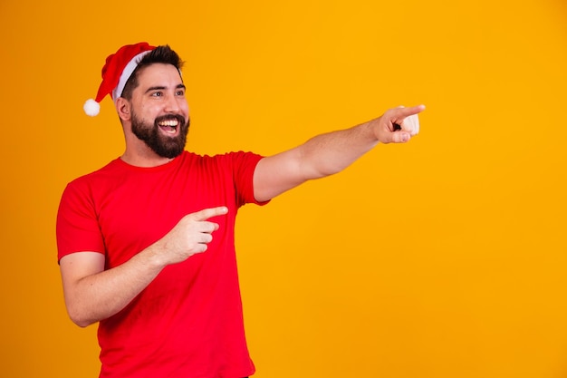 Bell'uomo vestito per natale che indossa il cappello di babbo natale che punta allo spazio di testo libero. promozione di fine anno