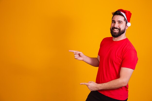 Bell'uomo vestito per natale che indossa il cappello di babbo natale che punta allo spazio di testo libero. promozione di fine anno