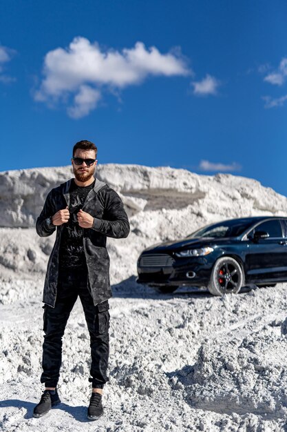 Bell'uomo vicino all'auto su uno sfondo di rocce bianche Elegante servizio fotografico