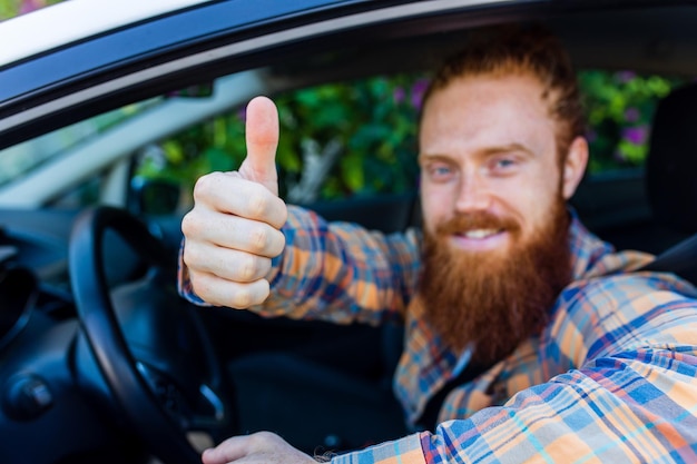 Bell'uomo zenzero dai capelli rossi con la barba lunga che va in viaggio durante le vacanze estive sulla nuova auto