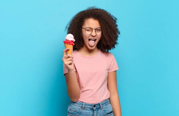 Bella adolescente afro con atteggiamento allegro, spensierato, ribelle, scherzando e tirando fuori la lingua, divertendosi. concetto di gelato estivo