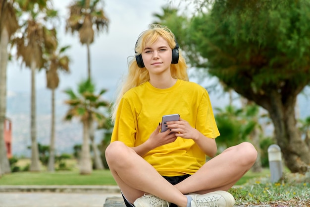 Bella adolescente femminile in cuffia con smartphone all'aperto