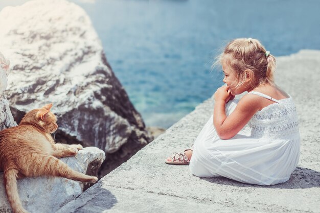 Bella adorabile bambina con gatto in riva al mare