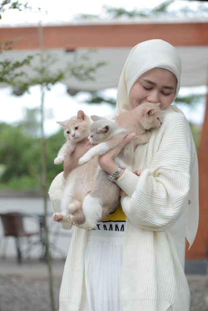 Bella asiatica musulmana amante dei gatti che gioca con il suo gatto all'aperto