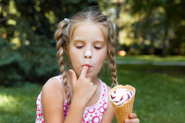 Bella bambina bionda che mangia il gelato in estate nel parco. ragazza allegra con gelato.