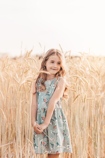 Bella bambina bionda con i capelli lunghi che cammina attraverso un campo di grano