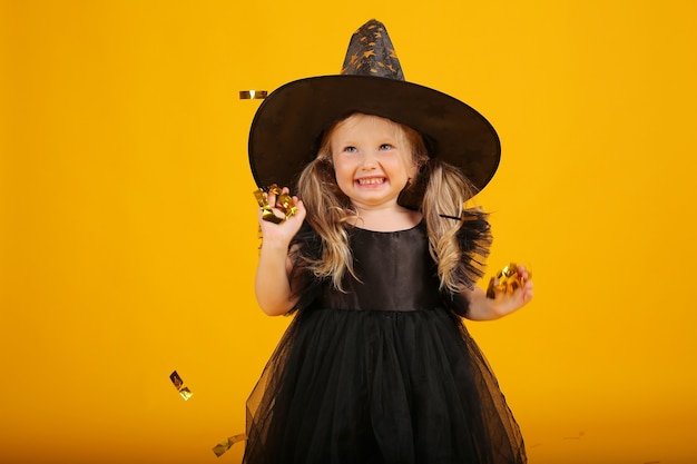 bella bambina bionda in un vestito nero e un cappello da strega halloween