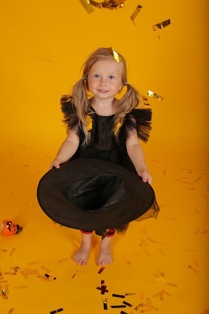 bella bambina bionda in un vestito nero e un cappello da strega halloween