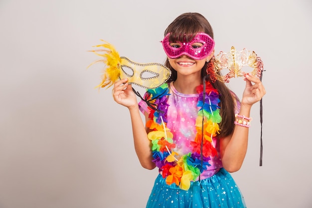 Bella bambina brasiliana vestita per il carnevale in Brasile con maschera di carnevale che tiene maschere che invitano alla festa