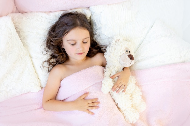 Bella bambina che dorme in un letto con un orsacchiotto