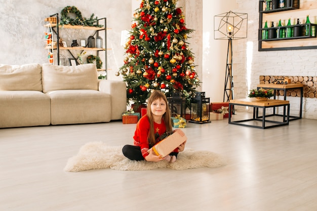 Bella bambina che gioca con un regalo di Natale, albero di Natale