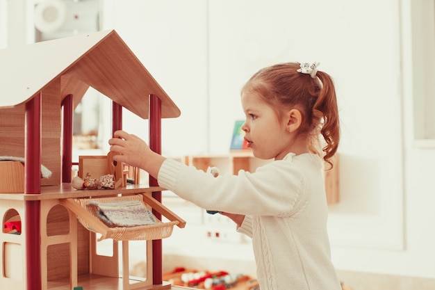 Bella bambina che gioca con una casa delle bambole in legno