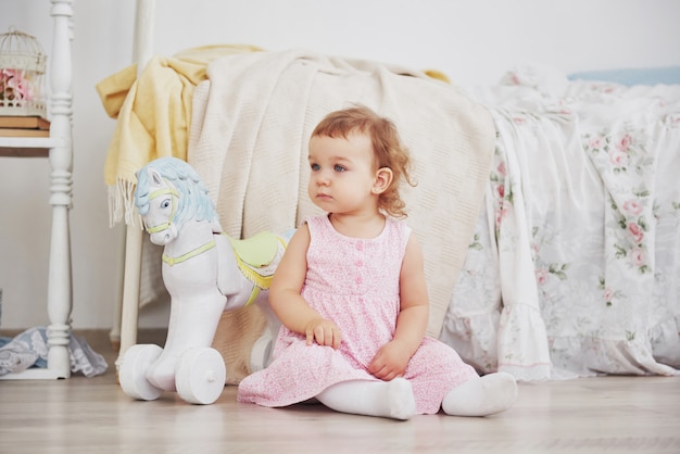 Bella bambina che gioca i giocattoli. Bionda dagli occhi blu. Sedia bianca. La stanza dei bambini. Ritratto di ragazza piccola felice. Concetto di infanzia