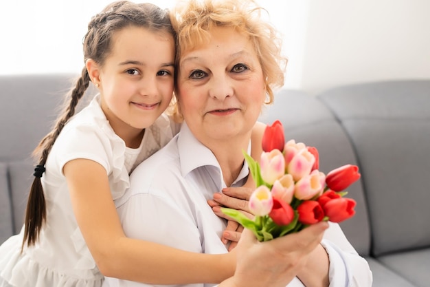 Bella bambina che presenta bouquet a sua nonna in una stanza luminosa.