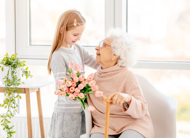 Bella bambina che presenta bouquet a sua nonna nella stanza leggera