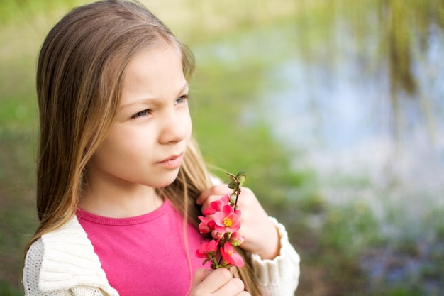 Bella bambina che tiene fiore di primavera nel parco e pensando.