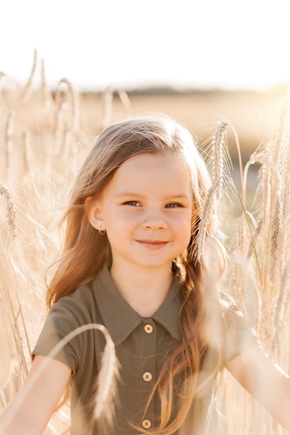 Bella bambina con i capelli lunghi che cammina attraverso un campo di grano in una giornata di sole. Ritratto all'aperto. Bambini che si rilassano