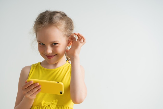 Bella bambina con lo smartphone che guarda avanti con un sorriso sornione tenendo la mano vicino all'orecchio fingendo di non sentire è abbastanza per giocare con il gadget