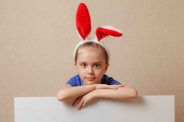 Bella bambina con orecchie da coniglio e banner bianco. Buona Pasqua