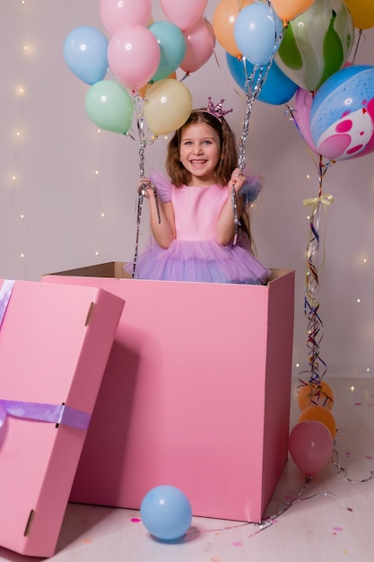 Bella bambina con palloncini salta fuori da un'enorme scatola rosa bambino festeggia il suo compleanno