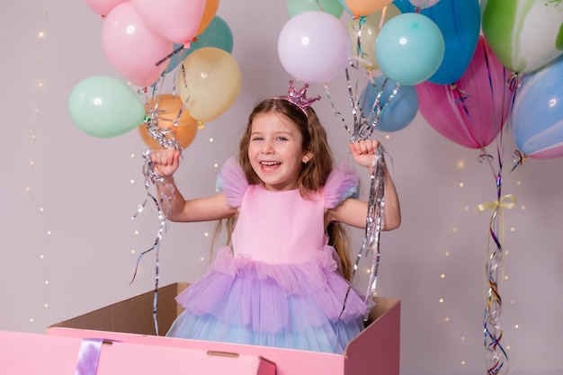 Bella bambina con palloncini salta fuori da un'enorme scatola rosa bambino festeggia il suo compleanno