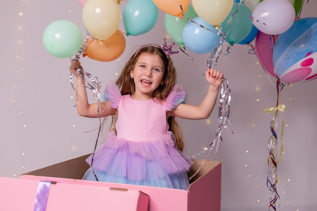 Bella bambina con palloncini salta fuori da un'enorme scatola rosa bambino festeggia il suo compleanno