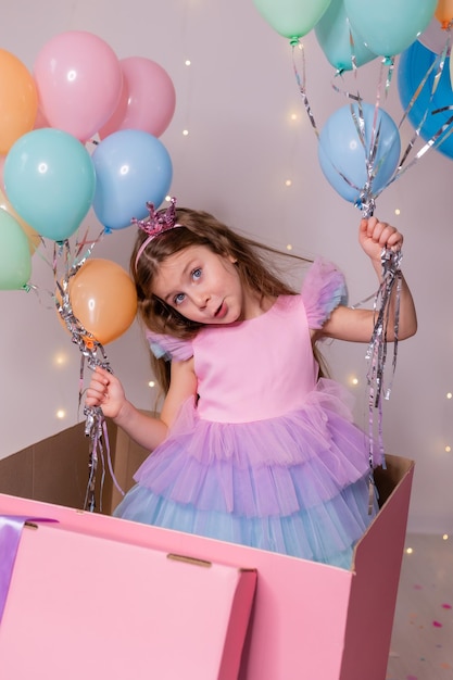 Bella bambina con palloncini salta fuori da un'enorme scatola rosa bambino festeggia il suo compleanno