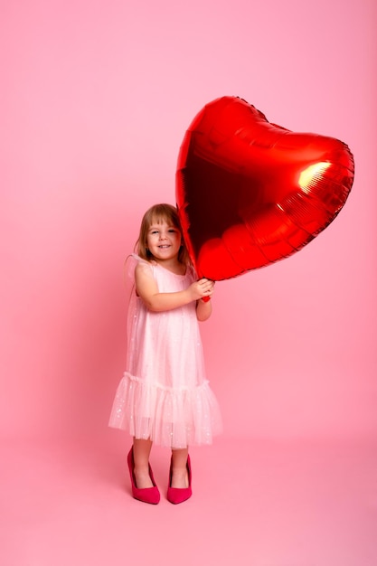 Bella bambina con palloncino grande cuore rosso su sfondo rosa che celebra il giorno di San Valentino