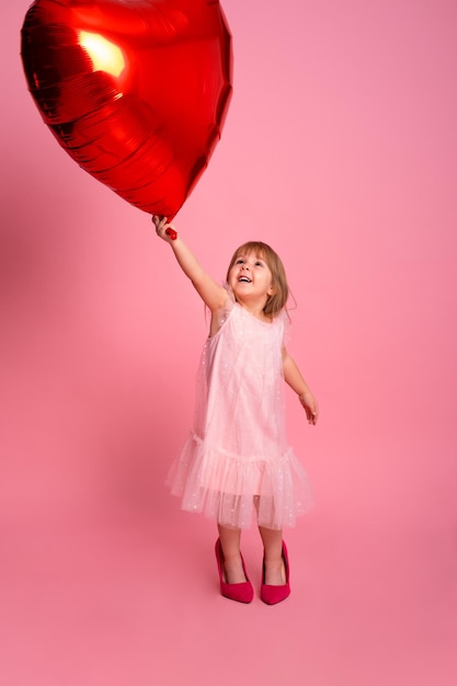 Bella bambina con palloncino grande cuore rosso su sfondo rosa che celebra il giorno di San Valentino