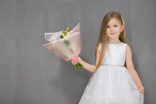 Bella bambina con un mazzo di fiori su uno sfondo grigio