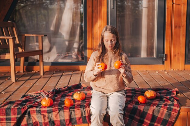 Bella bambina con zucche godendo la giornata autunnale sulla terrazza. Giorni di Halloween