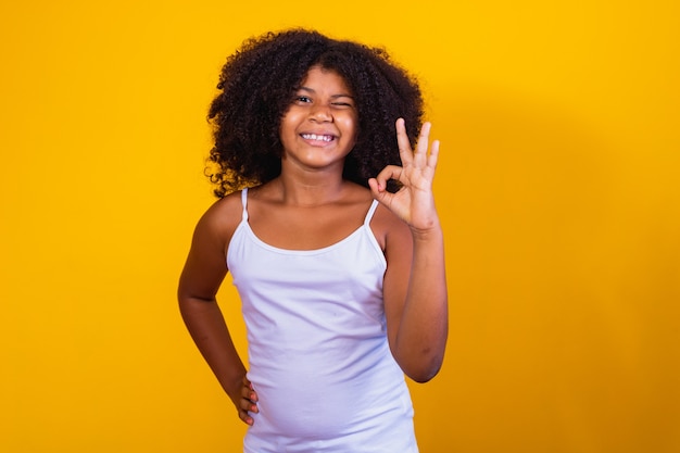 Bella bambina dai capelli ricci che usa il segno giusto delle mani. Sfondo giallo. Donna afro ok