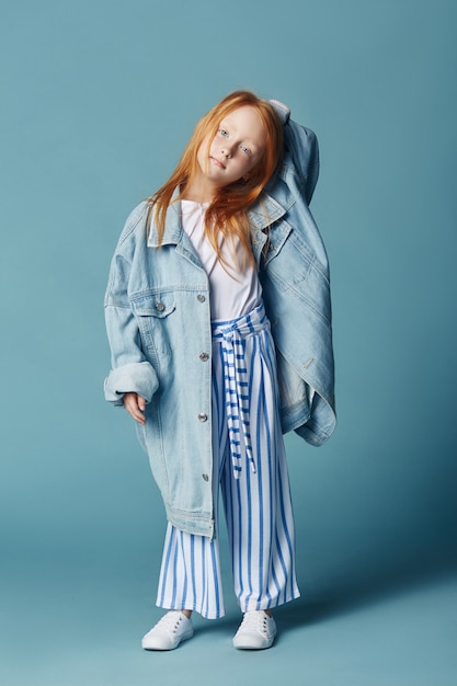 Bella bambina dai capelli rossi con i capelli lunghi in una grande giacca di jeans blu lungo.