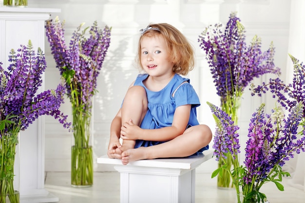 Bella bambina emotiva si siede tra i fiori viola. Una decorazione floreale in un interno