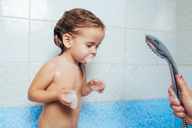 Bella bambina facendo un bagno. Un bambino gioca con acqua e spray dalla doccia.