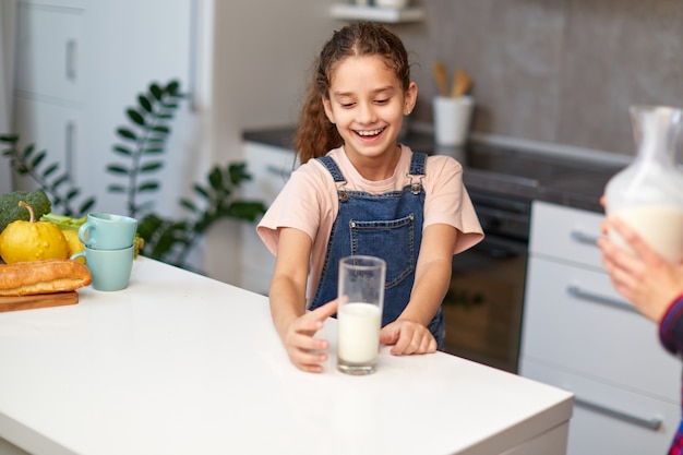 Bella bambina felice con un bicchiere di latte in cucina.