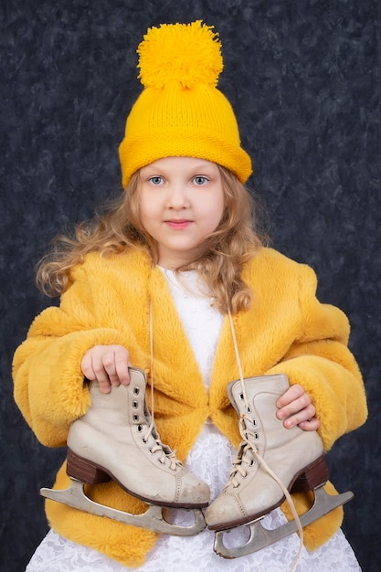 Bella bambina in abiti invernali con pattini bianchi. Bambino di cinque anni con un cappello giallo lavorato a maglia.