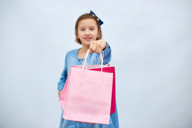 Bella bambina in abito casual in denim tenere in mano borse della spesa rosa