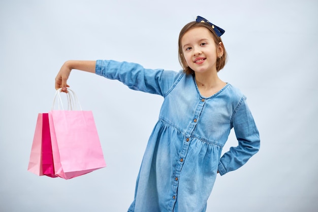 Bella bambina in abito casual in denim tenere in mano borse della spesa rosa