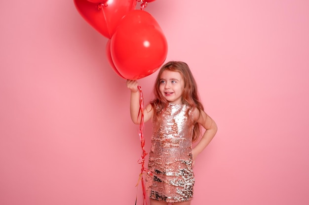 Bella bambina in abito con paillettes con palloncini romantici cuore rosso su sfondo rosa
