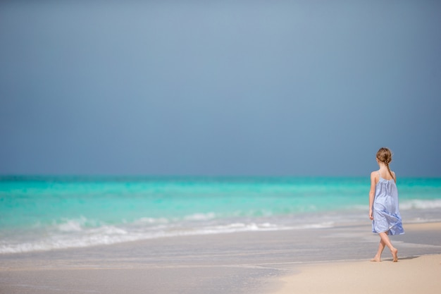 Bella bambina in abito in spiaggia divertendosi.