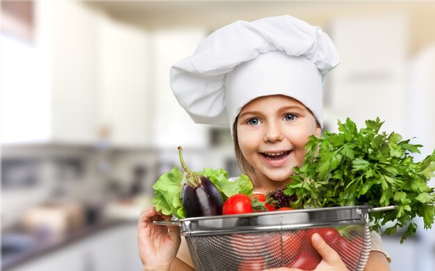 Bella bambina in cappello da cuoco che tiene ciotola con verdure