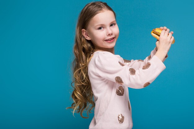 Bella, bambina in maglione con i capelli della brunetta in possesso di un hamburger