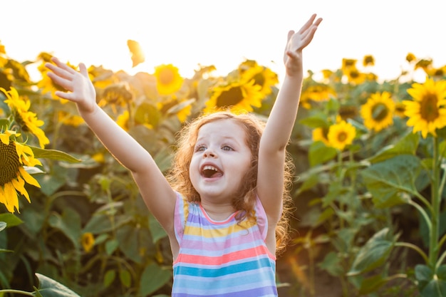 Bella bambina in piedi tra i girasoli e alzando le mani