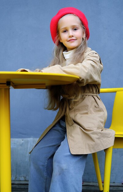 Bella bambina in un berretto rosso trench e jeans