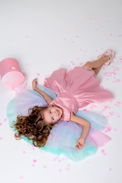 Bella bambina in un elegante vestito rosa giace sul pavimento cosparso di coriandoli vista dall'alto alla moda