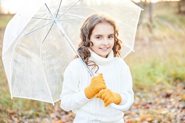 Bella bambina in un maglione bianco con un ombrello bianco in natura. Foto di alta qualità