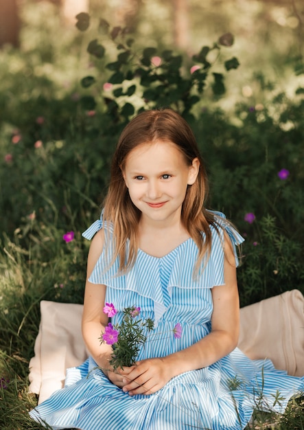 Bella bambina in un vestito blu con fiori in natura in estate