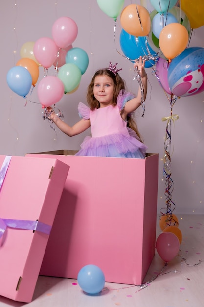 Bella bambina in un vestito colorato con palloncini sta giocando in un enorme bambino scatola sorpresa rosa